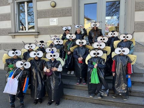 Kinder der Klassen 2a und 2b als Fliegen verkleidet als Gruppe vor dem Schulgebäude