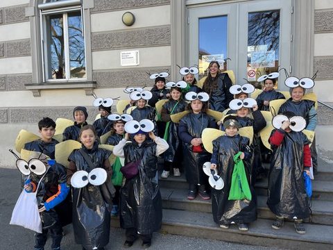 Kinder der Klassen 2a und 2b als Fliegen verkleidet als Gruppe vor dem Schulgebäude