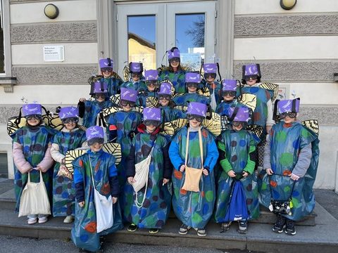 Kinder der Klassen 3a und 3b als Libellen verkleidet als Gruppe vor dem Schulgebäude