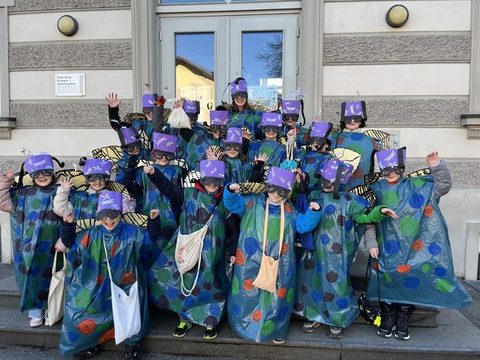 Kinder der Klassen 3a und 3b als Libellen verkleidet als Gruppe vor dem Schulgebäude