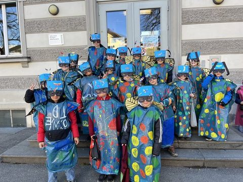 Kinder der Klassen 3a und 3b als Libellen verkleidet als Gruppe vor dem Schulgebäude