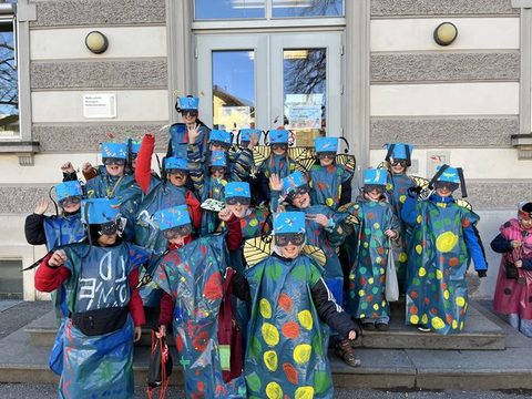 Kinder der Klassen 3a und 3b als Libellen verkleidet als Gruppe vor dem Schulgebäude